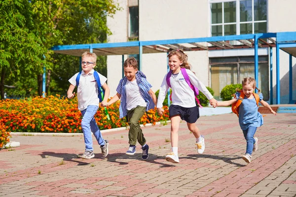 A group of school children running out of school, holding each ot — стоковое фото