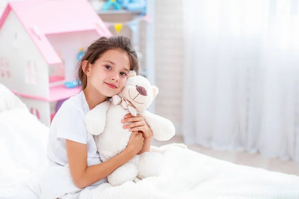 Щаслива весела молода дівчина сидить на ліжку тримає Тедді боа — стокове фото
