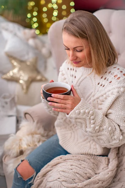 blonde girl in a sweater with a Cup of tea sitting on the bed