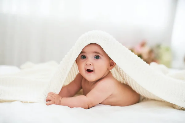 Baby under handduken. ett glatt litet barn ser ut från und — Stockfoto
