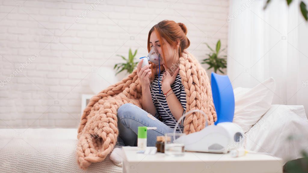 Young woman doing inhalation with a nebulizer at home