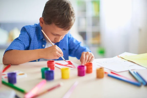 Il bambino disegna con una spazzola vernici ad acquerello su carta il lett — Foto Stock