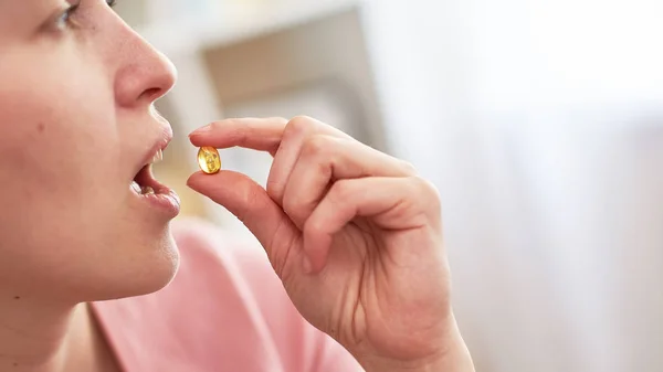 a woman takes a tablet with fish oil in capsules.