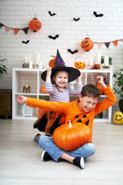 Cadılar ve balkabakları gibi giyinmiş çocuklar, neşeyle el sallıyorlar.