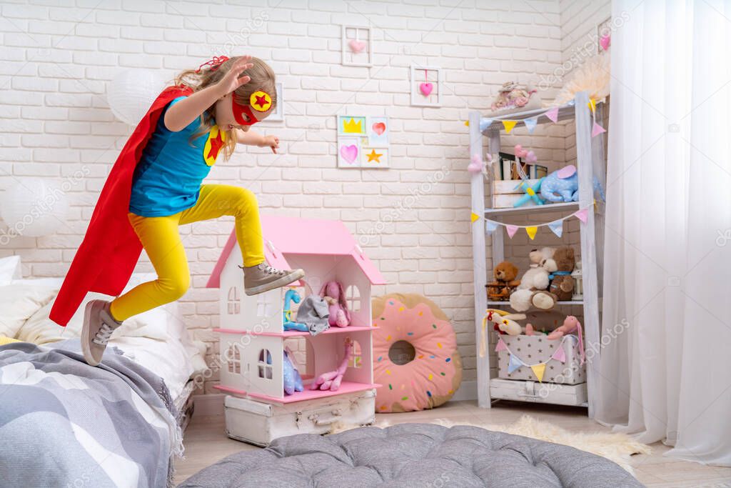 brave cute little girl jumps out of bed, imagining flight. child plays superhero with Cape and mask at home Saving world and fighting evil. concept of protectors and saviors in person small child.