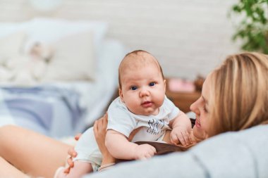Mutlu, sevgi dolu anne küçük oğluyla birlikte kanepede oturuyor. Sarıl ve bebekle konuş. Kadın gülümser, çocukla oynar ve ona bakar. Çocuk ilginç bir şekilde çerçeveye bakıyor. Annelik kavramı.