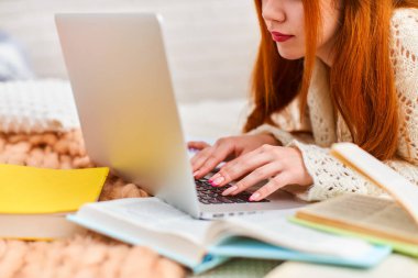 Yatakta yatarken ev ödevi yapan yakın bir öğrenci. Genç kız internette dizüstü bilgisayarla çalışıyor, sınavlara hazırlanıyor, uzaktan öğrenme, koronavirüs karantinasında kendini eğitme, e-öğrenme.