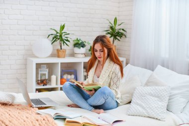 Öğrenci yatakta yatarken ödev yapıyor / Genç ve güzel bir kız dizüstü bilgisayarla çalışıyor, sınavlara hazırlanıyor, uzaktan öğrenme, koronavirüs karantinasında kendini eğitme, e-öğrenme.