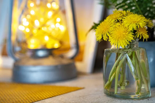 Home cozy atmosphere, on the table is a glass jar with a bouquet of dandelions. Medicinal plant of yellow color with a pleasant aroma, lifts mood. The concept of comfort in the house, spring peace.