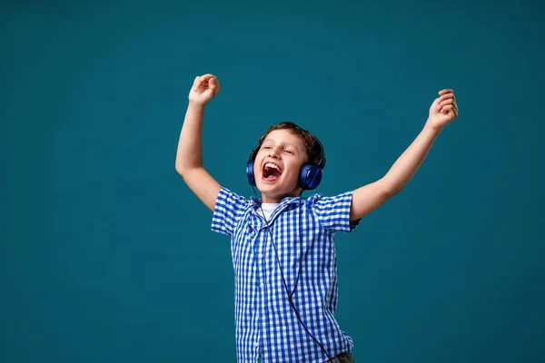 Full of emotions. Enjoying the song playing in your headphones. A small child does vocals on a song, a big music fan. Karaoke and entertainment. I join the song on a blue background.