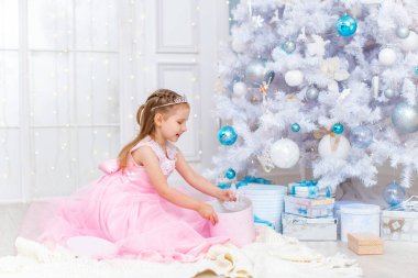 Mutlu Noeller ve tatiller! Süslü elbiseli şirin küçük kız ve taç hediyeleri açıyor. Hediye kutularıyla ağacın altındaki çocuklar. Noel oyuncaklarıyla dekore edilmiş oturma odası. Beyaz Saray 'da sıcak bir kış günü.