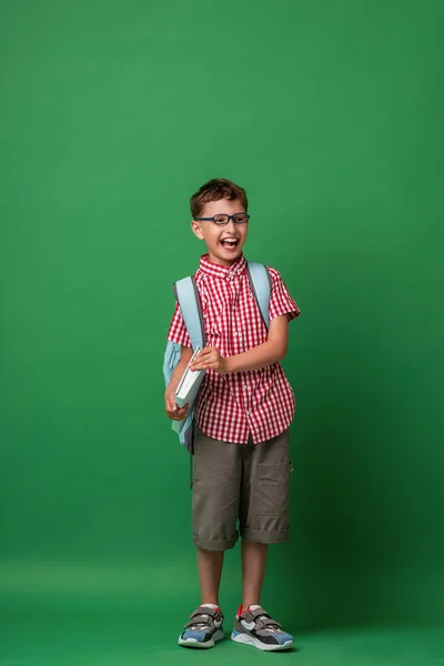 面白いスマート白人の少年7学校の袋と本とメガネで歳 現代のバックパック 子供は笑って緑の背景に長さのポーズをとっています 学校で初めて 学校に戻る — ストック写真
