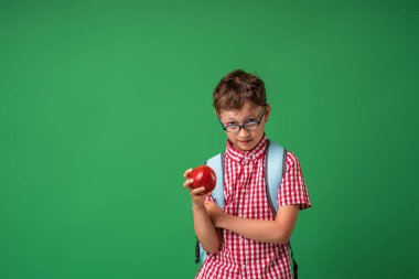Ciddi bir özenli çocuk elinde kitap ve bir Apple tutuyor, kurulun arka planında duruyor. Akıllı bir çocuk okula geri döner. Yeşil bir arka planda izole edilmiş. Bilgiye yönlendir