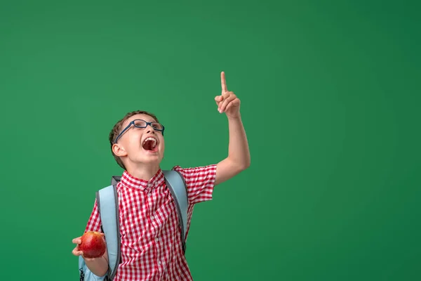 陽気でいたずら好きな少年は 緑のボードの背景に立って 彼の手にアップルを保持しています 興奮した子供は自由空間に注意を向けます 学校に戻る — ストック写真