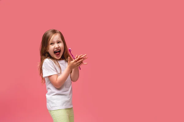 一个快乐的小女孩 喜欢刷牙 笑着带着健康的白牙 表现出一种赞许的姿态 带着粉红的背景上课 口腔卫生 每天刷牙2次 — 图库照片