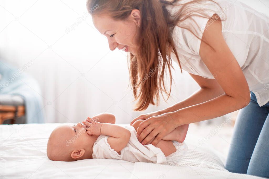 Happy loving family. A young mother is lying on the bed with a small child. the woman smiles, plays and hugs the baby. the concept of motherhood.