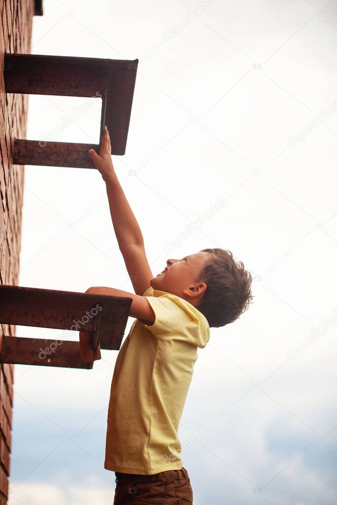 teenage boy climbs a brick wall to the roof. Child in danger. Climbs on a construction site in an unfinished building. Danger of falling from a height.