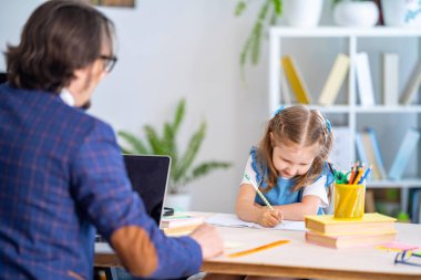 Şirin küçük kız evde bir öğretmenle ders alıyor. İlkokul öğretmeni. Anaokulu eğitimi. Babam ödevlerine yardım ediyor. Bireysel eğitim.