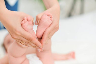 Yatağın üzerinde çocuk ayak masajına yakın çekim. Bir anne yeni doğmuş şirin bir bebeğin ayağına masaj yapar. Çocuğun bacağına odaklan..