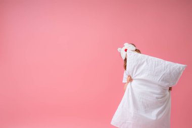 Uyku maskeli sevimli küçük kız bir yastığın arkasına saklanıyor, neşeyle gülüyor ve pembe bir arka planda poz veriyor. Sağlıklı uyku kavramı. Boşluğun bir kopyası.