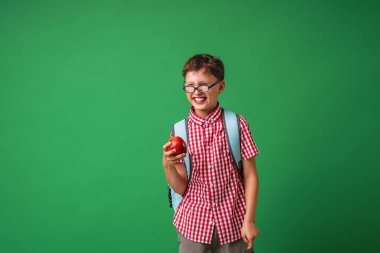 Neşeli, yaramaz çocuk elinde bir elma tutuyor ve kurulun arka planında durup gülüyor. Olumlu bir çocuk okula döndüğü için mutludur. Yeşil bir arka planda izole edilmiş. Okula geri dön..