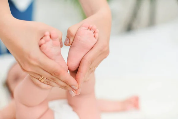 Close-up of children\'s foot massage on the bed. A mother massages the foot of a cute newborn baby\'s foot. Selective focus on the child\'s leg.