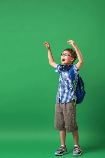 Happy cute smart boy in glasses with school bag and headphones. Modern backpack. child tries to see through glasses on a green background. Vision problem. Poor vision. First time at school. Back to school.