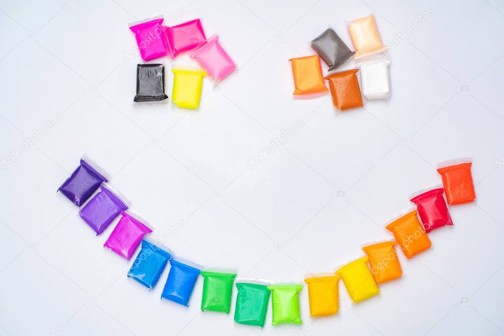 Air plasticine mass for modeling colored ultralight plasticine on a white background. Plasticine is laid out in the color of the rainbow, in the form of a smile.