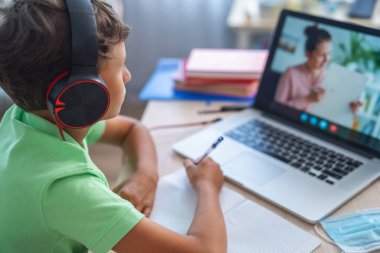 Küçük çocuk öğretmeniyle video görüşmesi yapmak için kulaklıklı dizüstü bilgisayar kullanıyor. Ekran, dersten konuyu açıklayan öğretmenle çevrimiçi ders gösteriyor. E-Eğitim Mesafesi Öğrenme, Ev Eğitimi.