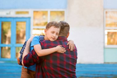 Mutlu aile babası ve oğlu. Adam çocuğuna sarılıyor, ilkokul öğrencisi. Babam okuldan sonra okul çocuğuyla tanışır. Okula dönelim. Okula gitmeden önce sarılalım. Çocuk babasını sıkıca ve sevgiyle kucaklıyor ve gözlerini kapıyor..