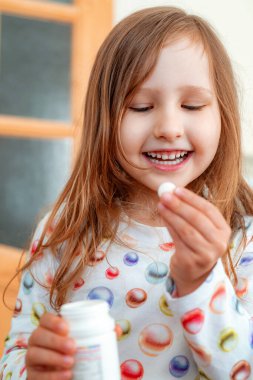 Küçük kız vitaminleri alır, kavanozdan tablet alır ve ağzına koyar. Çocuk çiğneme vitaminleri, belli elementler ve mineraller. Gerekli gelişmeler için kullanışlı. Hipervitaminosis. Hipovitaminoz.