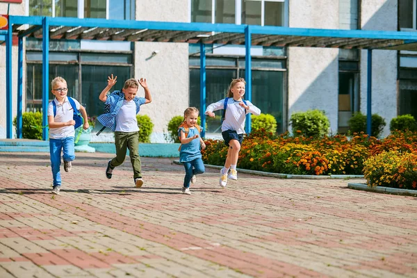 group of school children with backpacks run out of school, after the end of classes. Classmates, school friends. The beginning of holidays. The end of quarantine. Back to school.