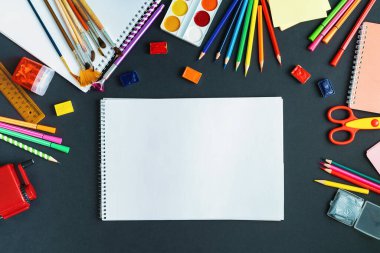 Okul malzemeleri kara tahta arka planında sergileniyor. Merkezde, siyah bir yüzey üzerinde, bir albüm var, uzayı kopyalamak için bir yer. Suluboya, kalem, keçeli kalem, fırça ve çizim malzemeleri. Okula geri dön..