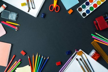 Okul malzemeleri kara tahta arka planında sergileniyor. Merkezde, siyah bir yüzeyde, uzayı kopyalamak için bir alan var. Suluboya, kalem, keçeli kalem, fırça ve çizim malzemeleri..