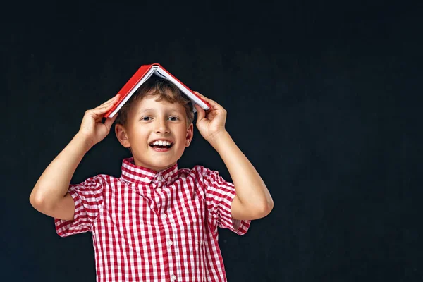 Портрет Смішний Усміхнений Хлопчик Книгою Голові Позує Чорному Тлі Підготовка — стокове фото