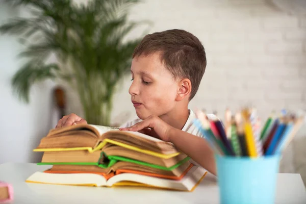 Back to school. An attentive boy is sitting on a table with a stack of books. A student studies textbooks. Thirst for knowledge. The child is passionate about doing homework.
