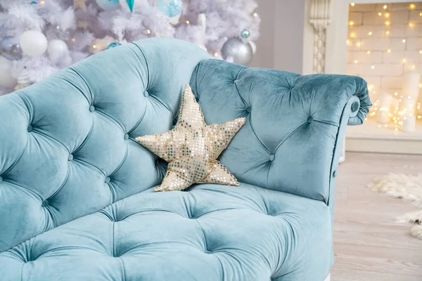chic turquoise sofa with a heart-shaped sequin pillow. against the background of a room decorated for Christmas with a beautiful white Christmas tree and an elegant fireplace with bokeh lights.