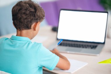 Yüksek açı mesafesi evde dizüstü bilgisayardan öğreniyor. Yan görünüm çocuğu, Notepad 'den beyaz ekranlı notlar alır, ses dersleri, uzaklık ve e-öğrenim kavramlarını dinler.