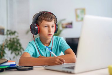 Kulaklık takan bir öğrenci karantina döneminde uzak mesafe öğrenimi için dizüstü bilgisayar kullanır. Çocuk çevrimiçi öğrenmekten bıktı. E-Eğitim Uzaklık Öğrenimi, Ev Eğitimi. Evde kal..