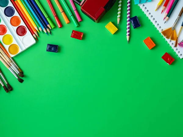 School supplies are displayed on a green background. In the center, on the green surface, there is a free space, a place to copy space. Watercolors, pencils, markers, brushes, and drawing supplies.Back to school.