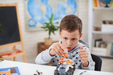 Yedi yaşında tatlı bir çocuk, bir okul çocuğu, müteahhitle eğleniyor, ödev yapmak yerine masada oturuyor. Kaliteli motor becerilerin gelişimi. Karantina sırasında evde öğrenim.