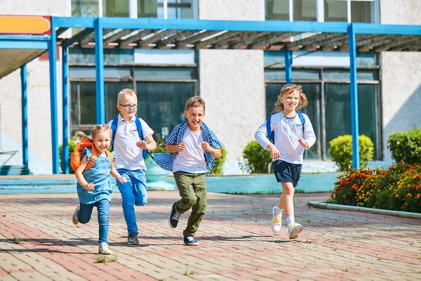 group of school children with backpacks run out of school, after the end of classes. Classmates, school friends. The beginning of holidays. The end of quarantine. Back to school.
