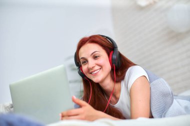 Kız öğrenci arkadaşlarıyla internet üzerinden iletişim kurmaktan mutlu. Evde eğitim, iş ve öğrenim, yeni bilgi. Yatakta bilgisayarla mutlu bir genç. Kadınlar yatakta dizüstü bilgisayara bakıp gülümsüyor..