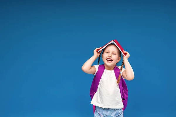 Glad Stygg Liten Skolflicka Med Ryggsäck Håller Bok Huvudet Poserar — Stockfoto