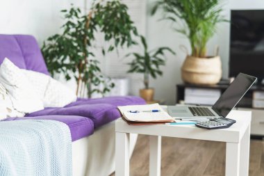 Kendini izole etme ve uzak mesafe öğrenme döneminde öğrencilerin işyeri. Kanepenin yanında küçük bir masa duruyor, üzerinde bir dizüstü bilgisayar ve çalışmak için yazılar var. E-öğrenme.