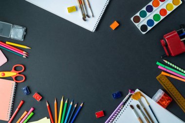 Okul malzemeleri karatahta arka planda sergileniyor. Merkezde, siyah yüzeyde kopyalama alanı var. Suluboya, kalem, keçeli kalem, fırça ve çizim malzemeleri. Okula geri dön.