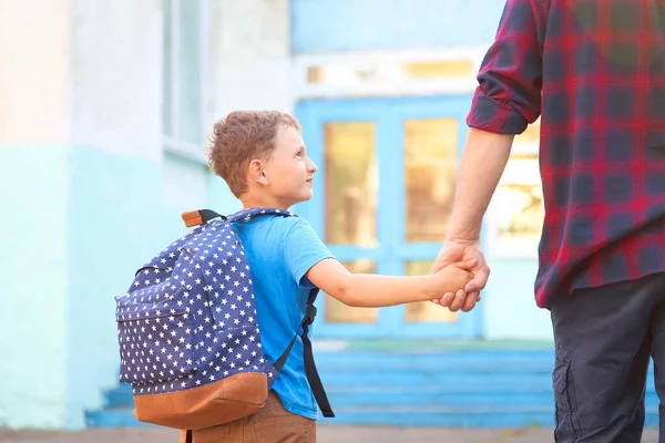 Dad walks the child to school. he encourages the student to accompany him to school. a caring father holds his son\'s hand tightly as he goes to school. a positive boy will be happy to go to primary school