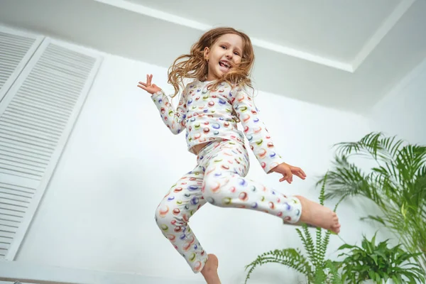 happy little girl jumps in her pajamas on the bed in the morning after a night\'s sleep. A positive start to the day. a happy lifestyle. A child jumps on his bed before going to sleep.