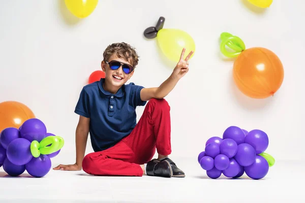 穿着太阳镜和时髦衣服的酷而时髦的男孩 坐在水果背景上 孩子们展示V符号 并在工作室的背景水果气球前摆出姿势 夏天的概念 维生素 — 图库照片