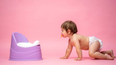 Bebek bezli şirin bebek lazımlığa emekliyor. Tuvalet ve tuvalet eğitimi. Küçük bir çocuk yararlı bir beceriye alışır. Hijyen. Bebek lazımlık lazımlığında oturuyor.